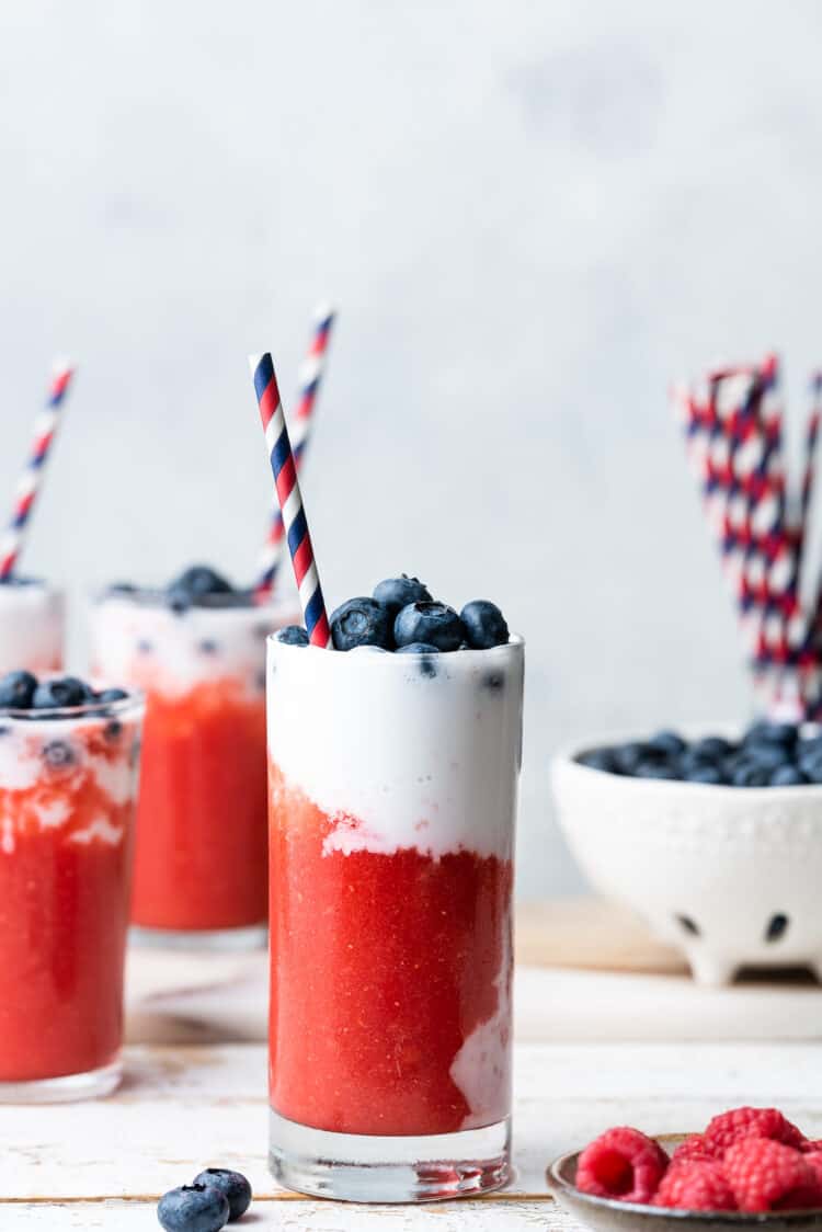 Slushies in tall glasses layered red and white and topped with fresh blueberries.