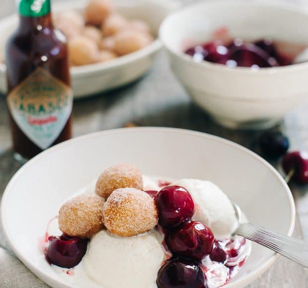 Churro Doughnut Holes with Ice Cream and Cherry Chipotle Sauce in a white bowl.
