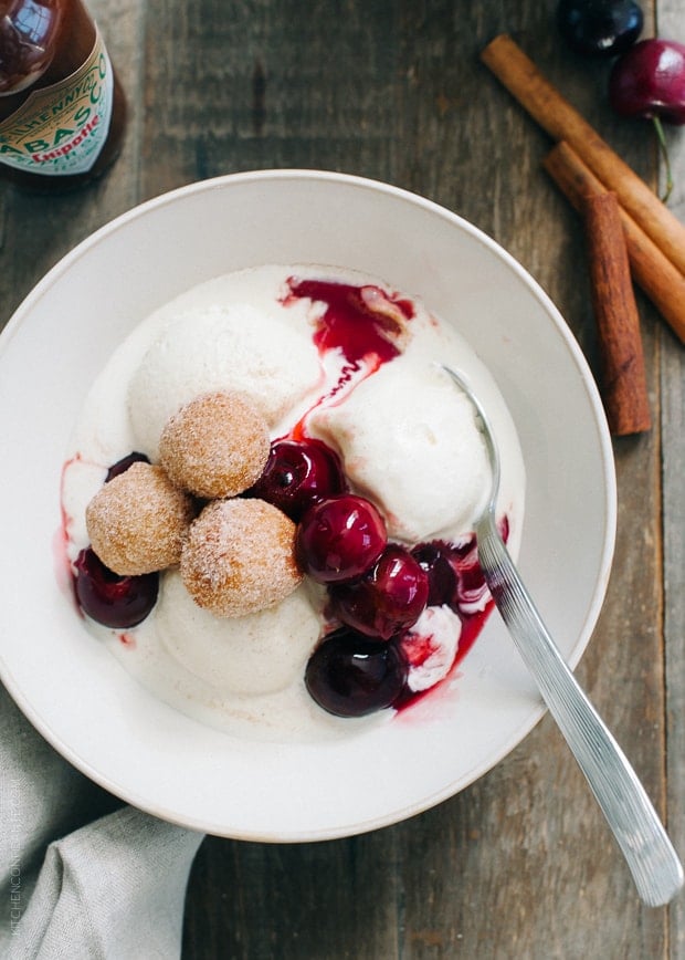 Churro Doughnut Holes with Ice Cream and Cherry Chipotle Sauce in a white bowl with a spoon.