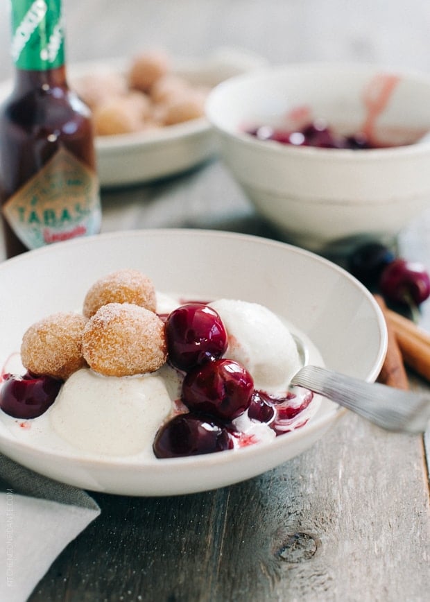 Churro Doughnut Holes with Ice Cream and Cherry Chipotle Sauce in a bowl on a wooden surface.