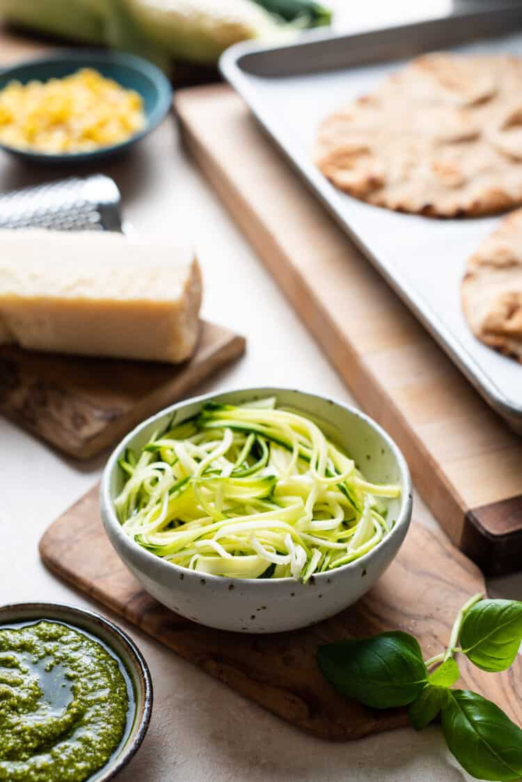 Swirls of shredded zucchini in a white bowl for Zucchini, Corn and Pesto Flatbreads.