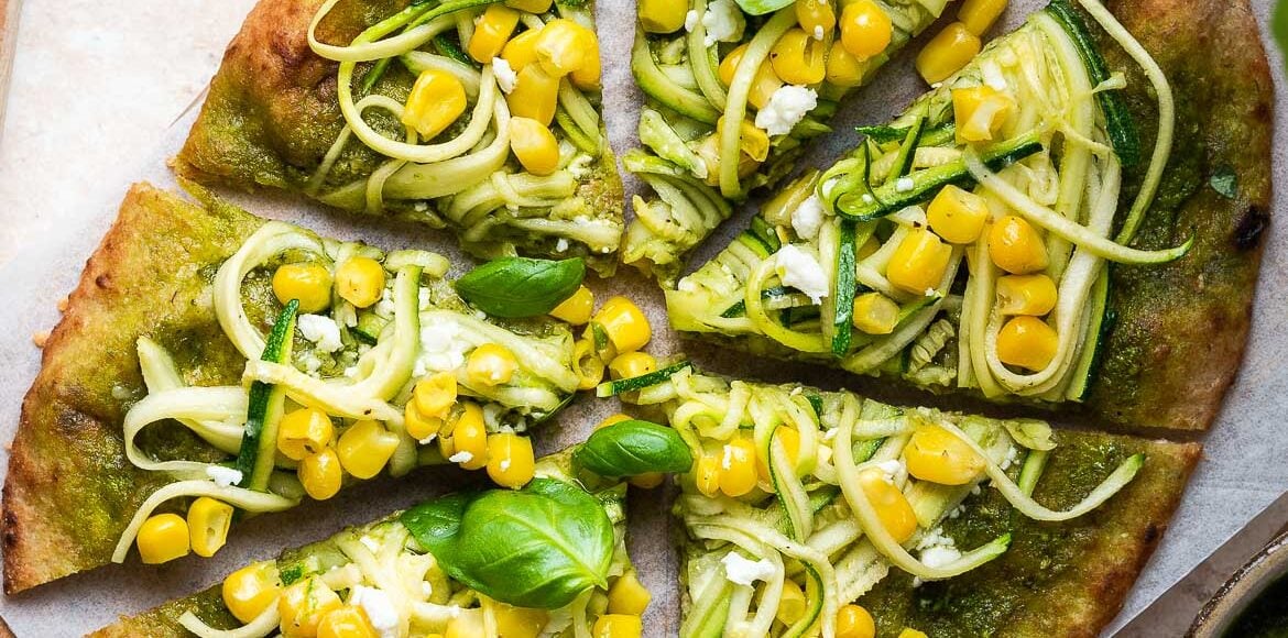 Zucchini, Corn and Pesto Flatbread sliced on a wooden board.