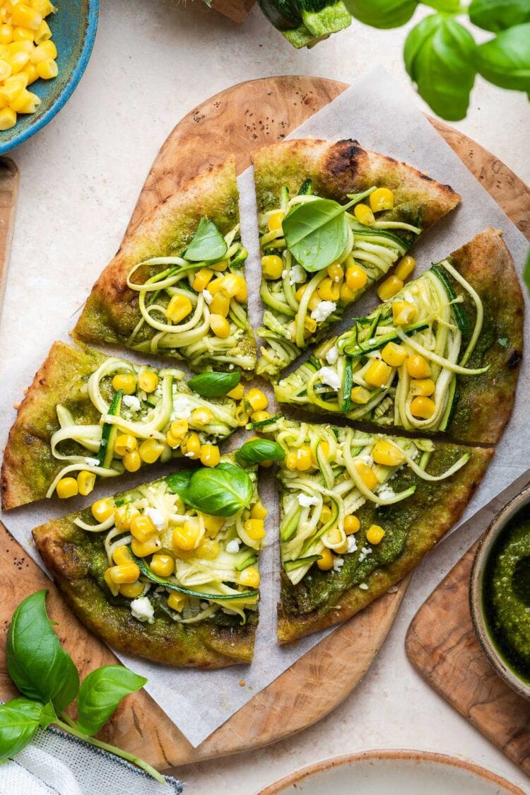 Zucchini, Corn and Pesto Flatbread sliced on a wooden board.