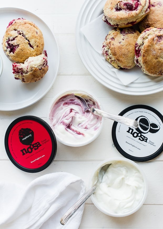 coconut raspberry scones on a white plate and white background with open containers of noosa yogurt