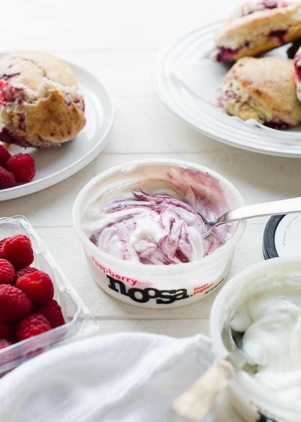 container of noosa raspberry yogurt with coconut raspberry scones and raspberries on a white background