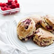 coconut raspberry scones on a white plate, raspberries in the background