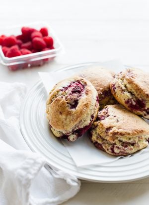 coconut raspberry scones on a white plate, raspberries in the background