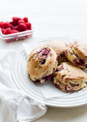 coconut raspberry scones on a white plate, raspberries in the background