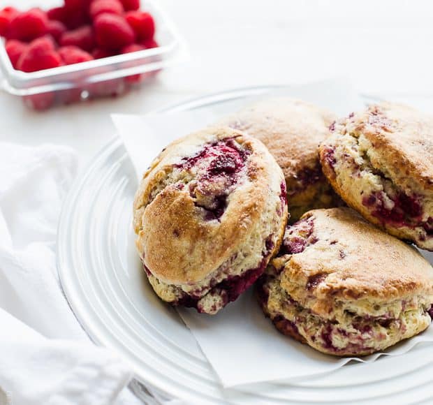 coconut raspberry scones on a white plate, raspberries in the background