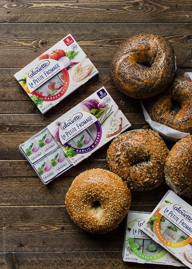 An array of bagels and spreadable cheese on a wooden surface.