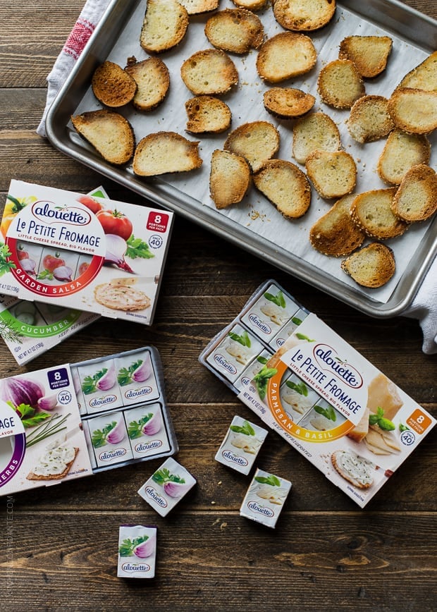 A baking tray of fresh-from-the-oven Garlic Parmesan Bagel Chips surrounded by a variety of spreadable cheese.