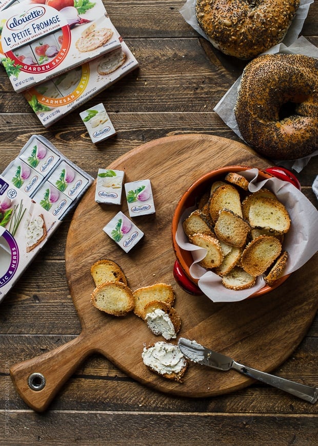 A baking tray of fresh-from-the-oven Garlic Parmesan Bagel Chips surrounded by a variety of spreadable cheese.