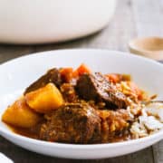Mechado, a Filipino Beef Stew, served over a bed of rice in a white bowl.