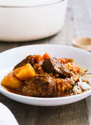 Mechado, a Filipino Beef Stew, served over a bed of rice in a white bowl.