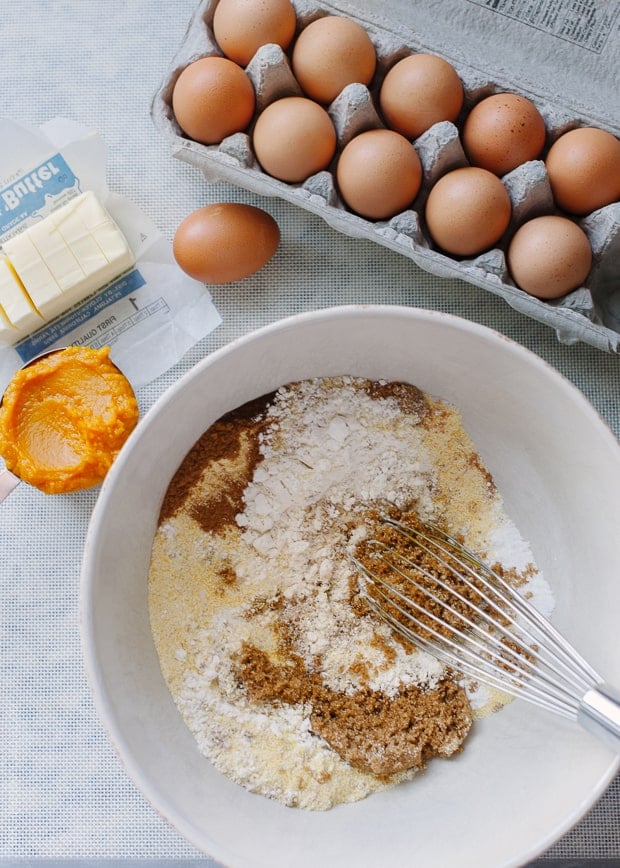 Bowl of dry ingredients for pumpkin scones surrounded by eggs, fresh pumpkin and butter.