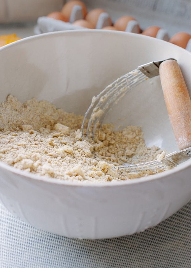 Pastry cutter in a white bowl filled with dry ingredients and butter. 