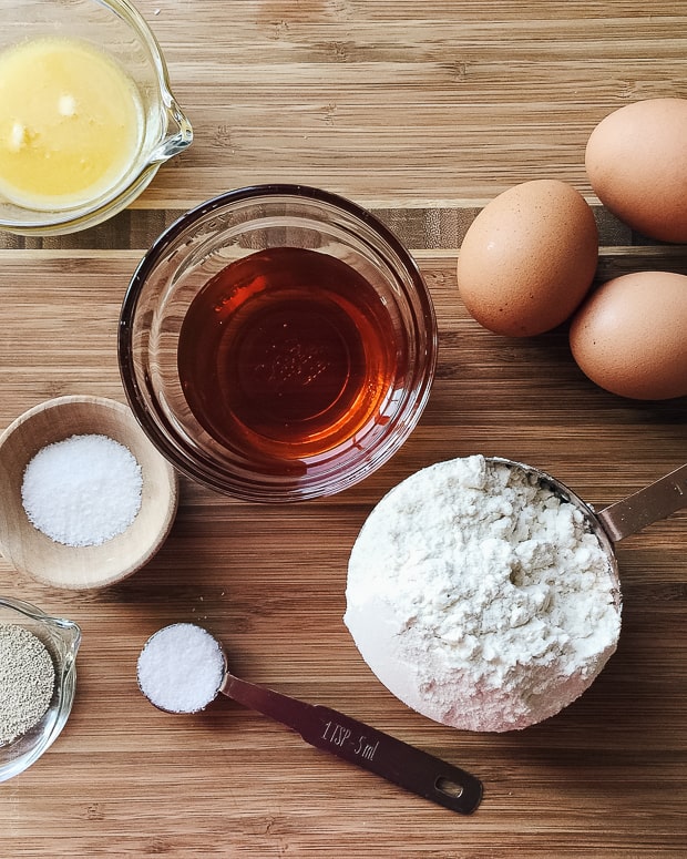 Flour, melted butter, honey, salt, sugar, yeast, and eggs assembled on a wooden surface.
