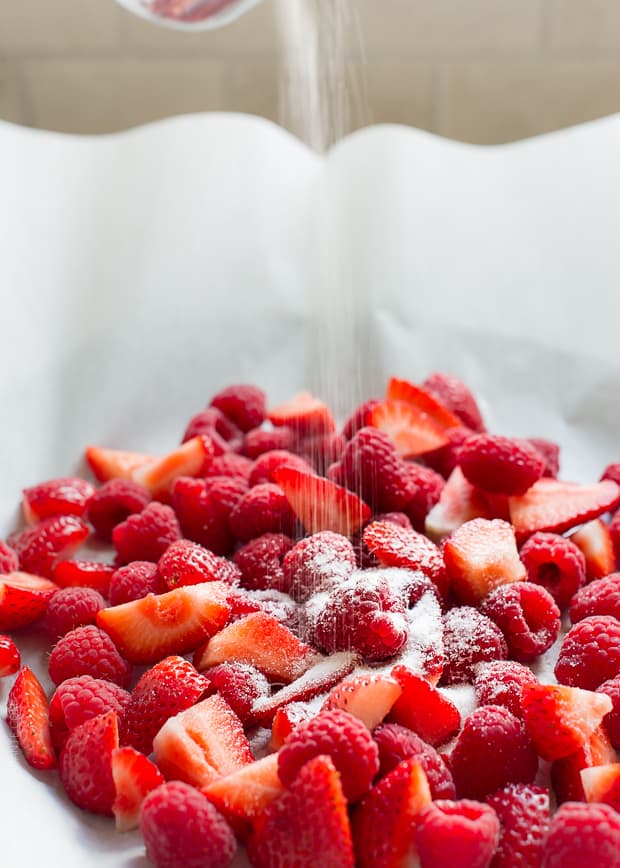 Sprinkling fresh strawberries and raspberries with sugar.