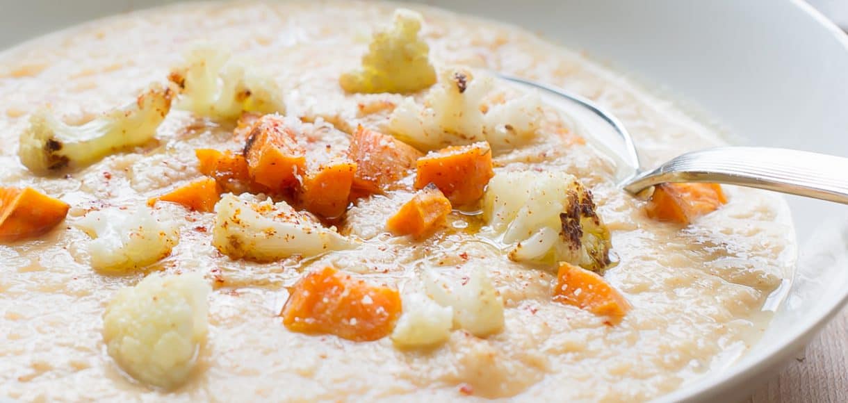 White bowl filled with Roasted Cauliflower and Sweet Potato Chowder and garnished with roasted cauliflower and sweet potatoes.