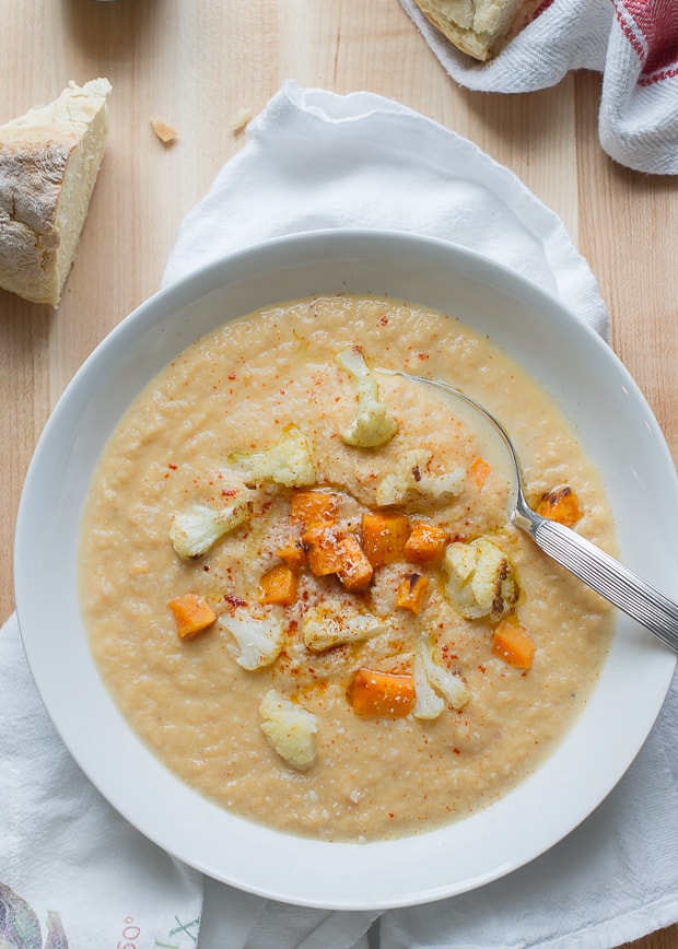 Roasted Cauliflower and Sweet Potato Chowder in a white bowl alongside a slice of fresh bread.