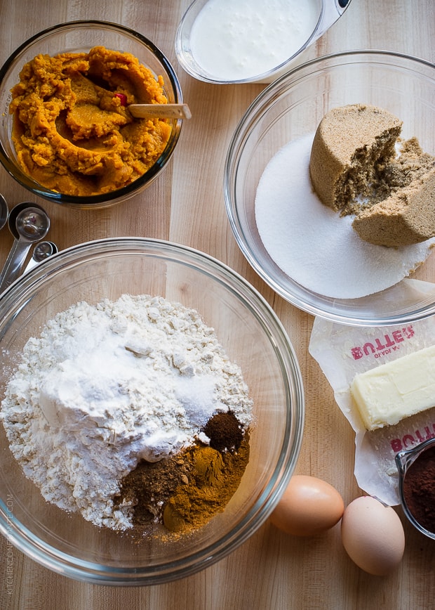 A bowl of pumpkin puree, a bowl of white and brown sugar, and a bowl filled with flour and spices on a counter top.