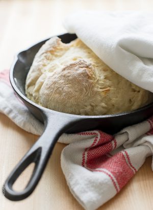 Skillet Soda Bread in a cast iron skillet with a red and ivory patterned kitchen towel alongside.