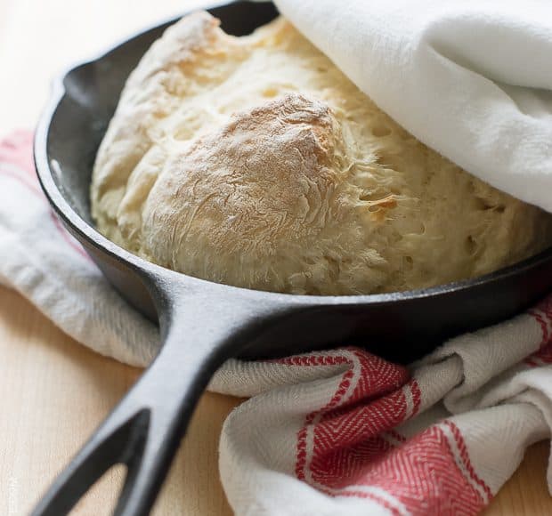 Skillet Soda Bread in a cast iron skillet with a red and ivory patterned kitchen towel alongside.