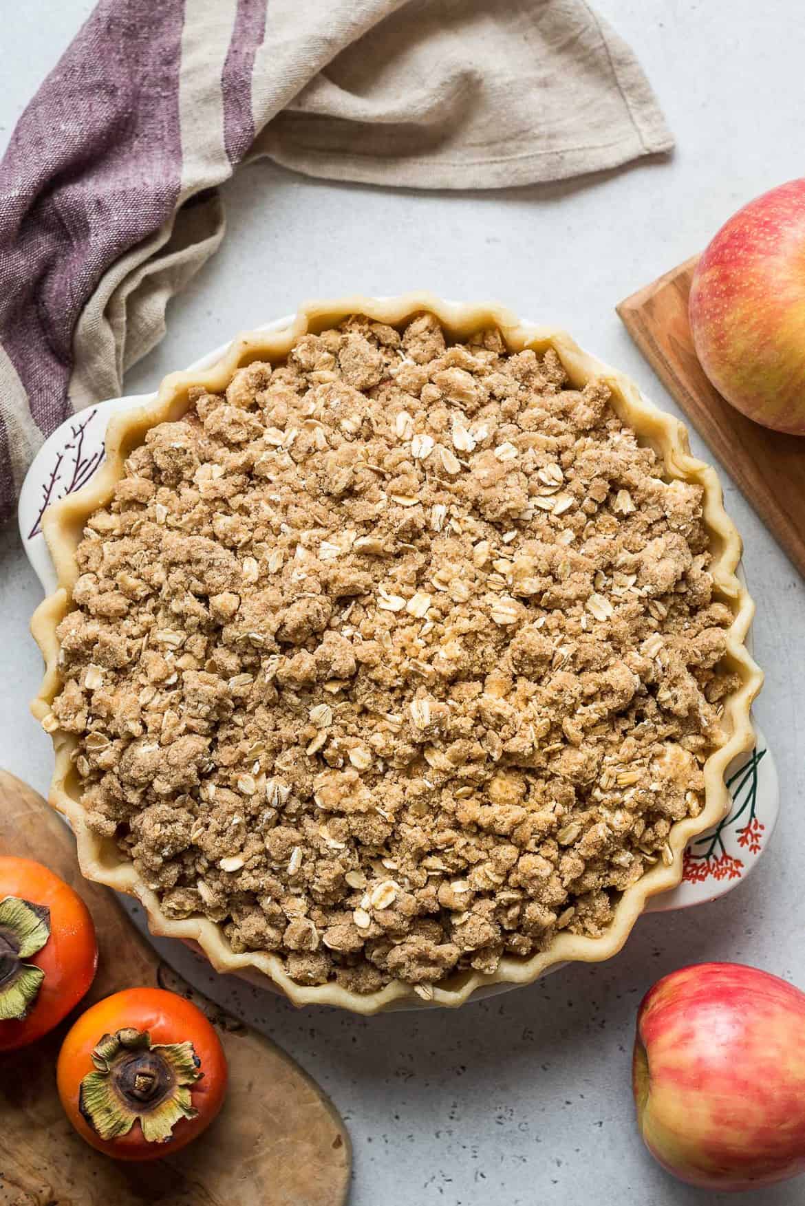 Chopped persimmons and apples under sweet oat streusel in a pie plate ready to bake.