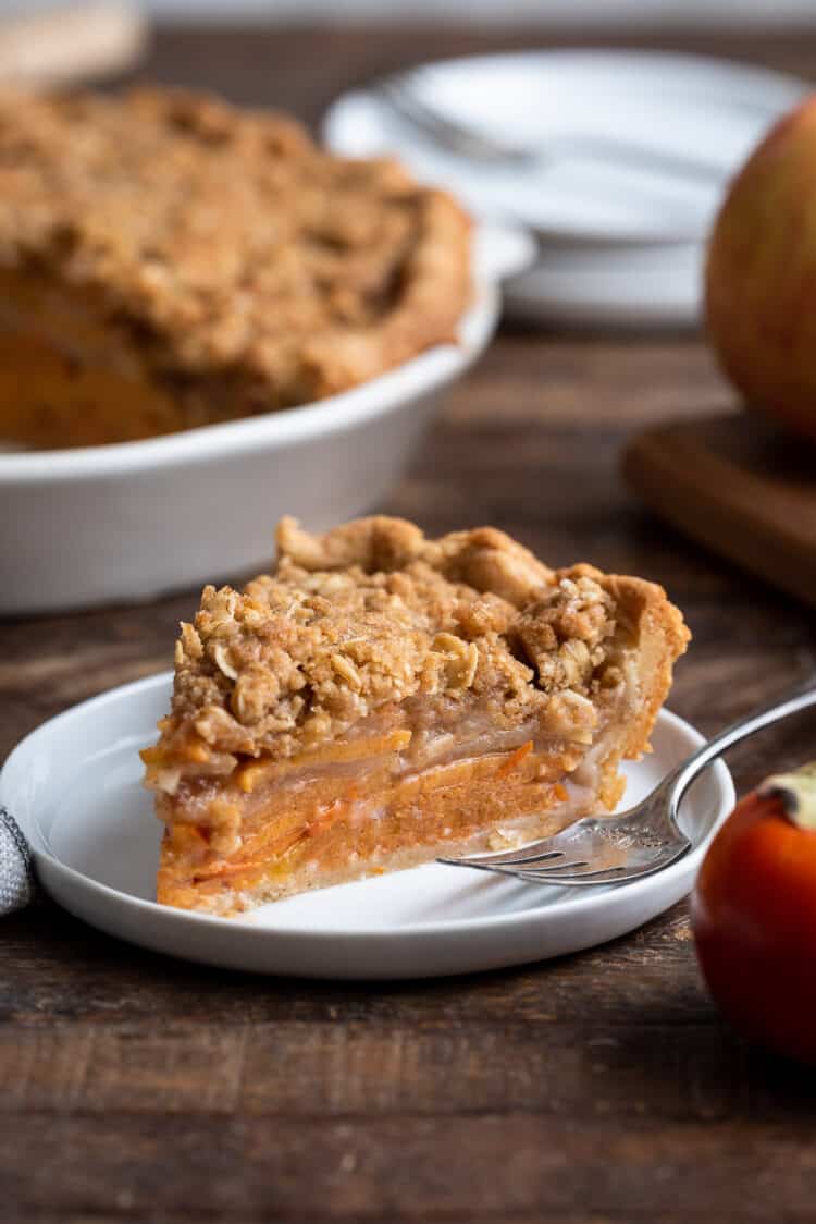 A slice of streusel topped Persimmon Apple Crumb Pie on a white plate.