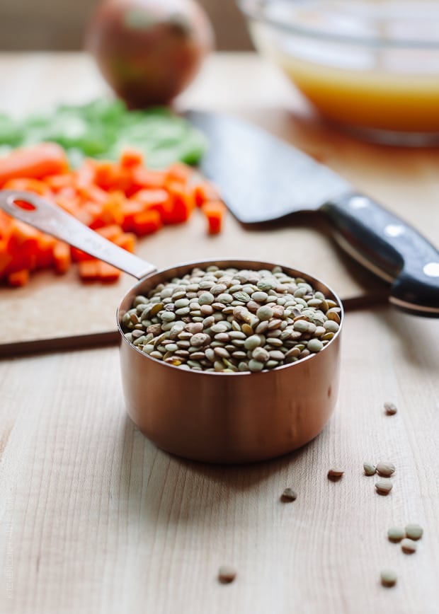 A measuring cup filled with lentils with diced vegetables in the background.