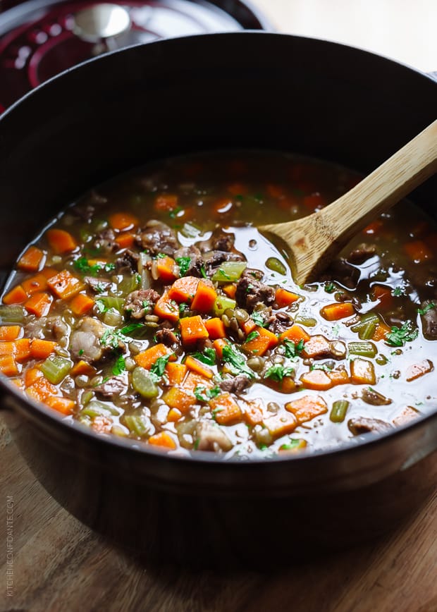 Stirring Prime Rib Beef and Lentil Soup with a wooden spoon in a large soup pot.