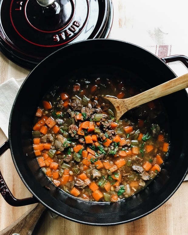 Stirring Prime Rib Beef and Lentil Soup with a wooden spoon in a large soup pot.