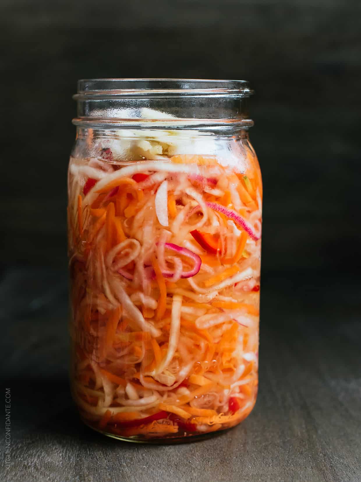 Glass jar filled with homemade Achara: Filipino Green Papaya Relish on a wooden surface.