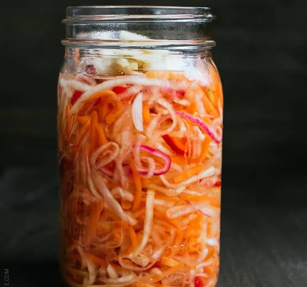 Glass jar filled with homemade Achara on a wooden surface.