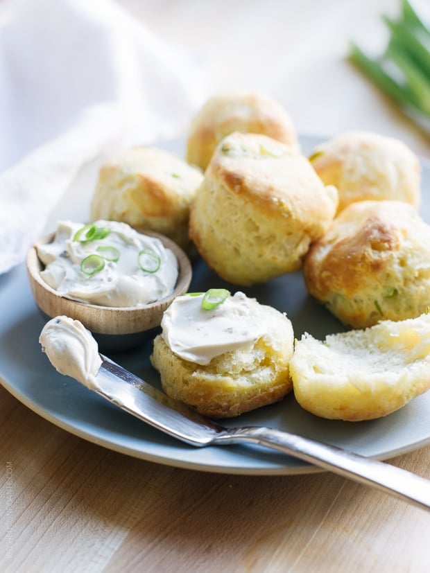 Cream Cheese and Green Onion Biscuits broken in half and slathered with soft cream cheese and garnished with green onions.