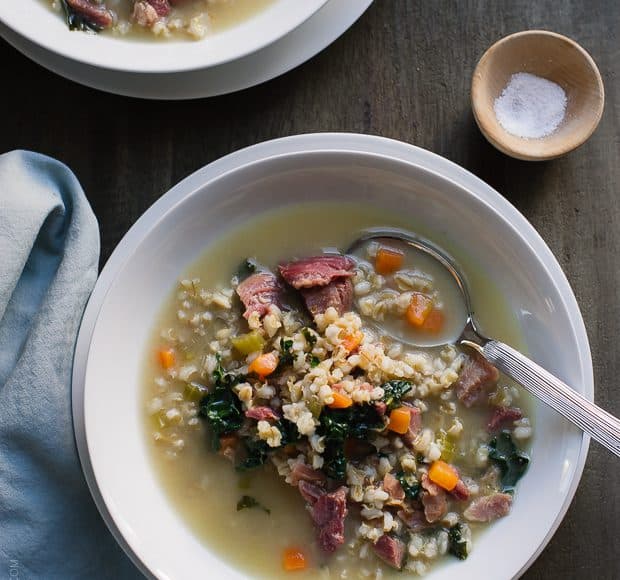 Two white soup bowls filled with Ham, Barley and Kale Soup made from a leftover ham bone.