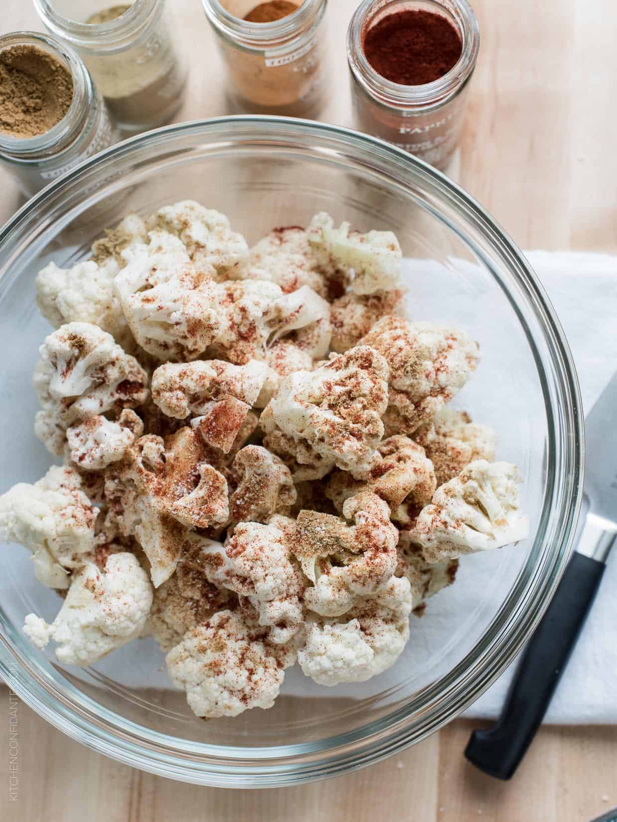 Cauliflower florets sprinkled with spices in a glass bowl. 