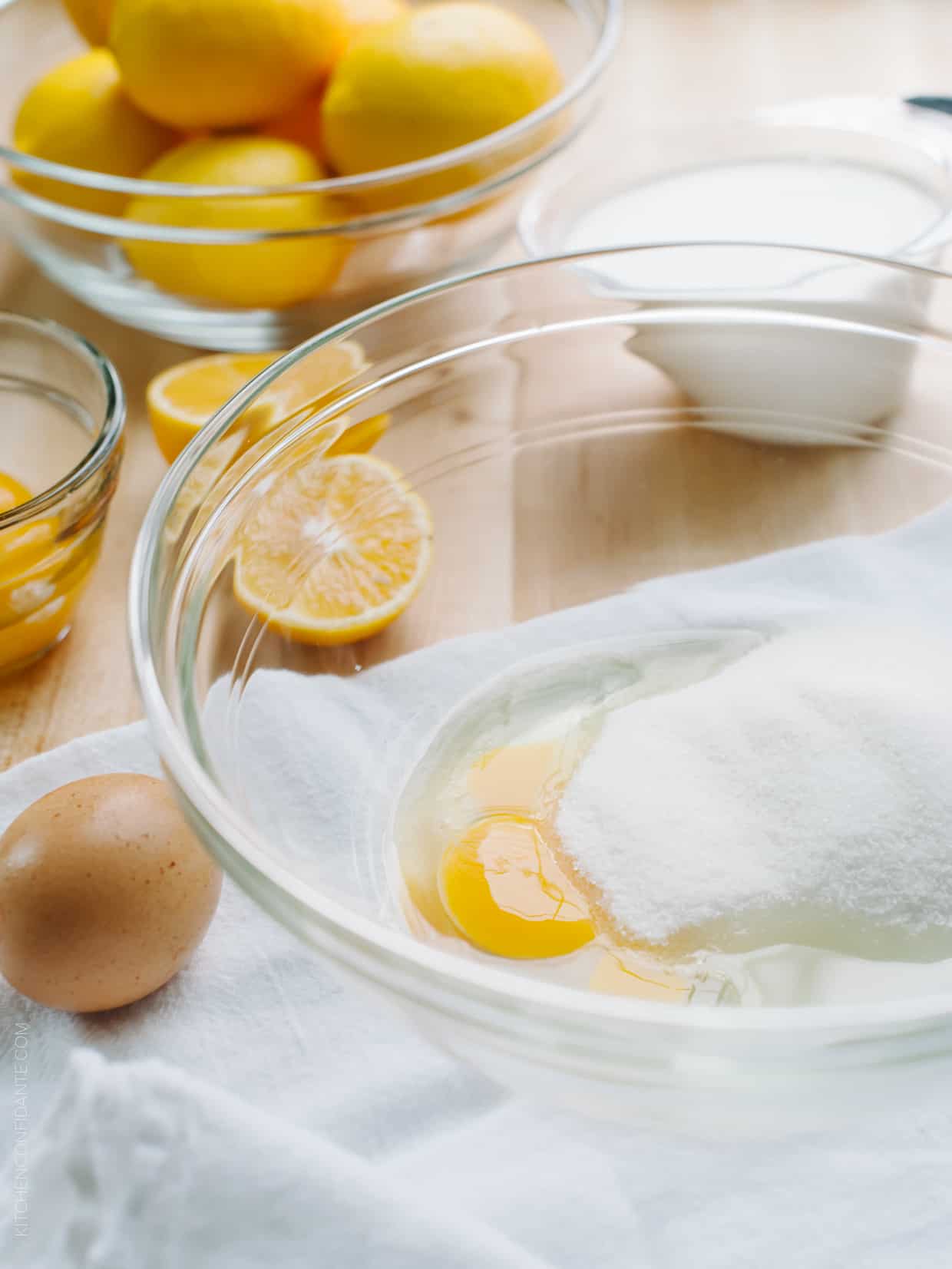 Sliced Meyer lemons alongside ingredients for a tart in a glass bowl.