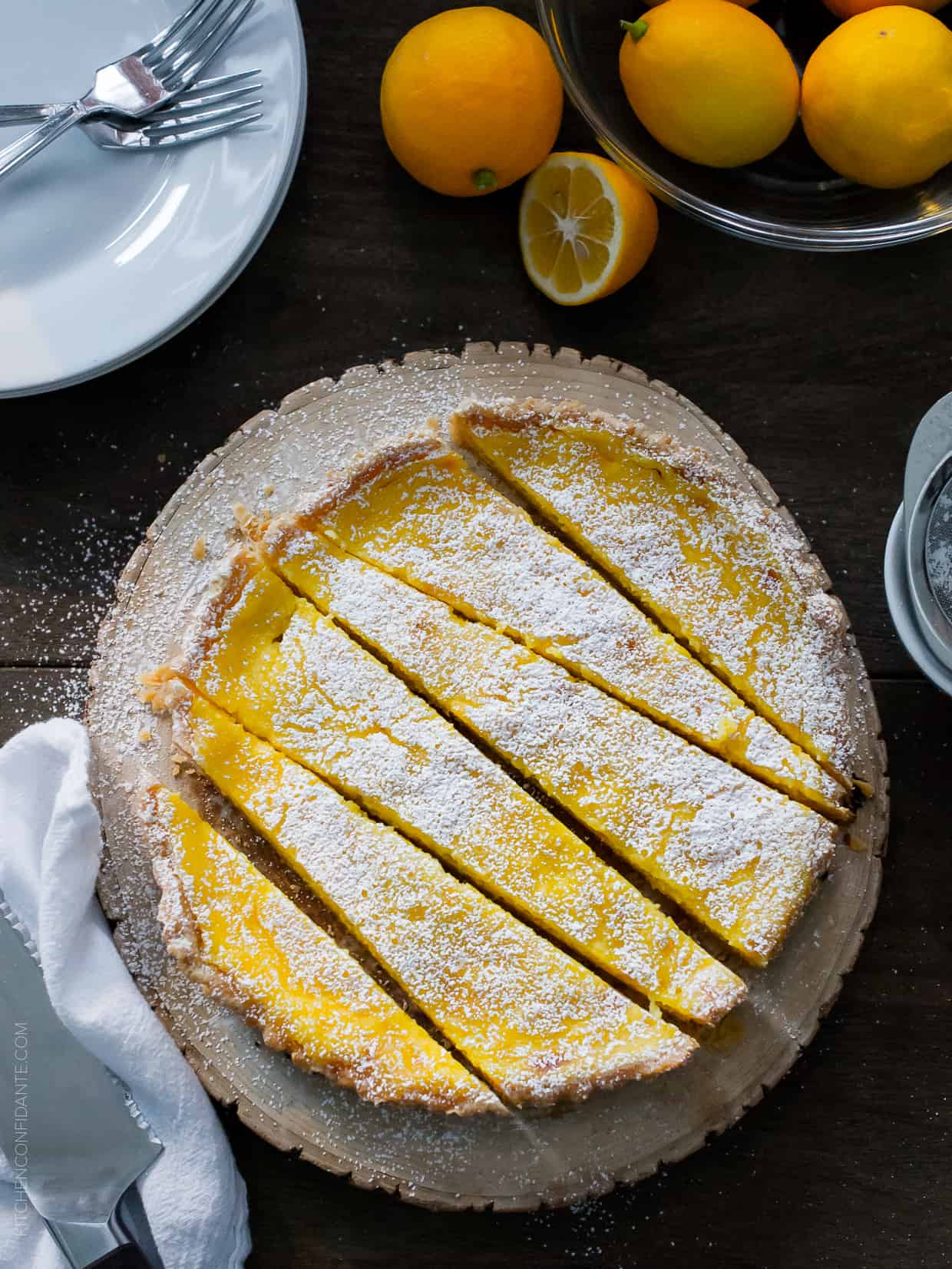 A Meyer Lemon Tart on a serving platter, sliced and dusted with powdered sugar.