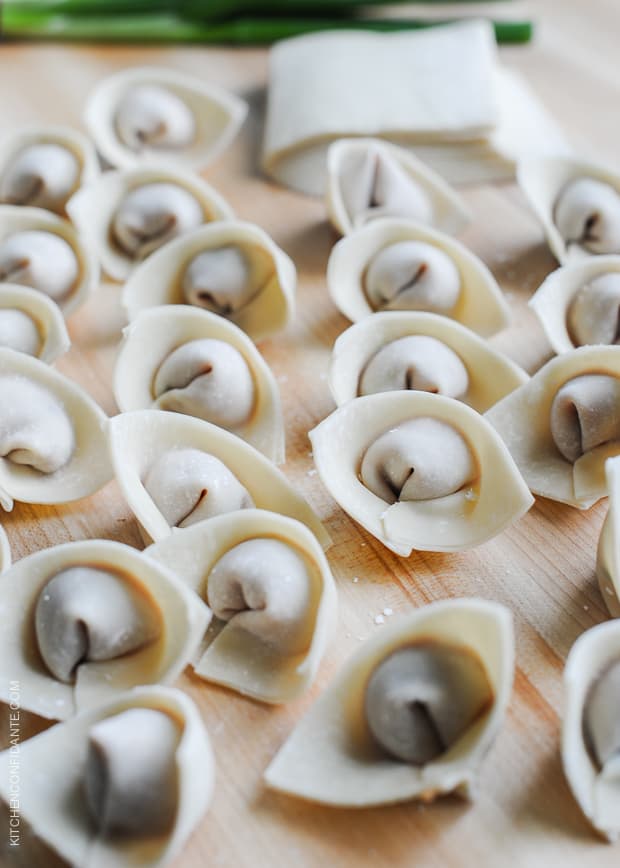 Filled wontons for wonton soup on a wooden surface.
