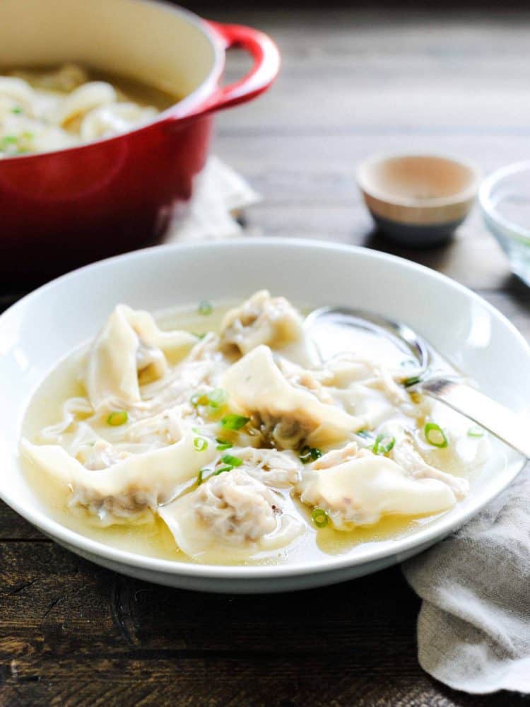 Sausage Molo Soup in a white bowl on a wooden surface, surrounded by a larger Dutch oven filled with soup.