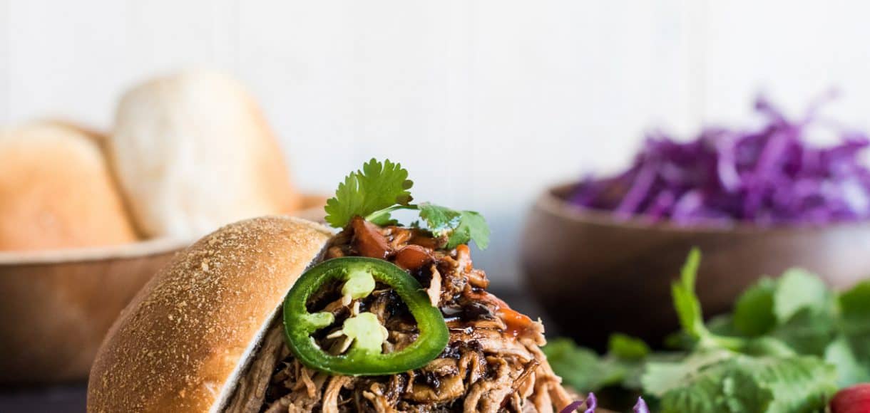 Filipino Adobo-style Pulled Pork Sandwich layered with red cabbage, a few leaves of cilantro and sriracha.