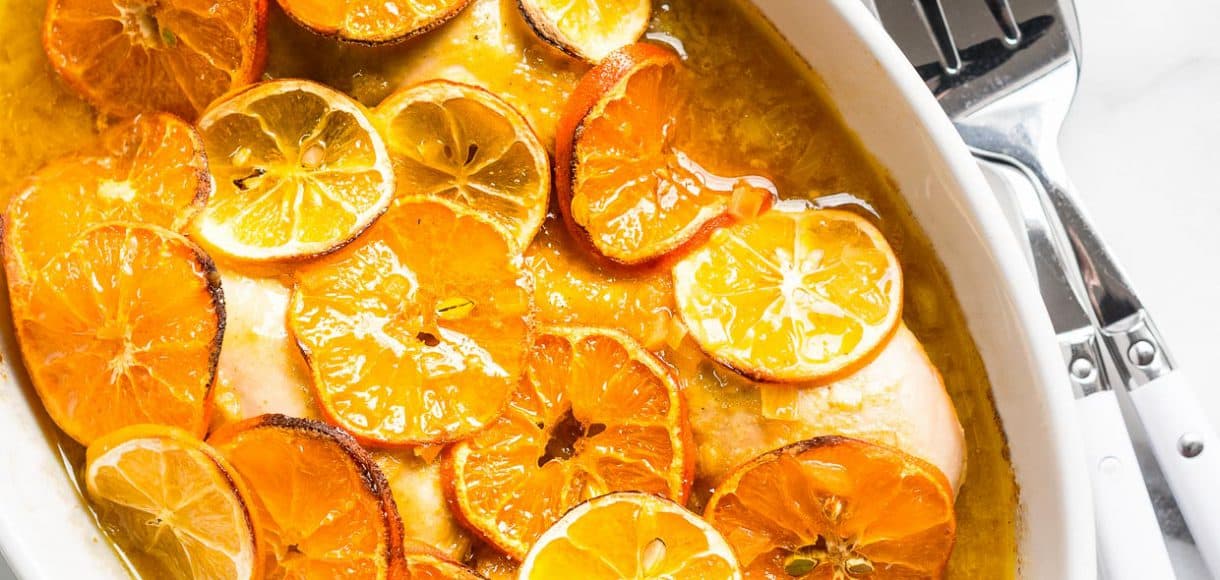 White baking dish filled with baked Honey Mustard Citrus Chicken and covered with slices of citrus fruit.