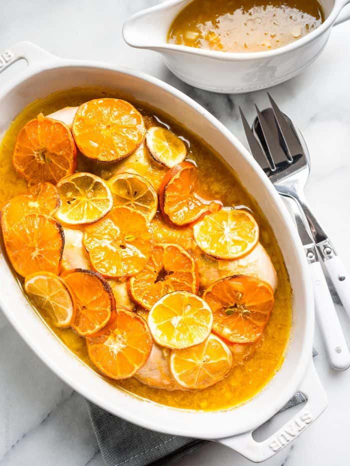 White baking dish filled with baked Honey Mustard Citrus Chicken and covered with slices of citrus fruit.