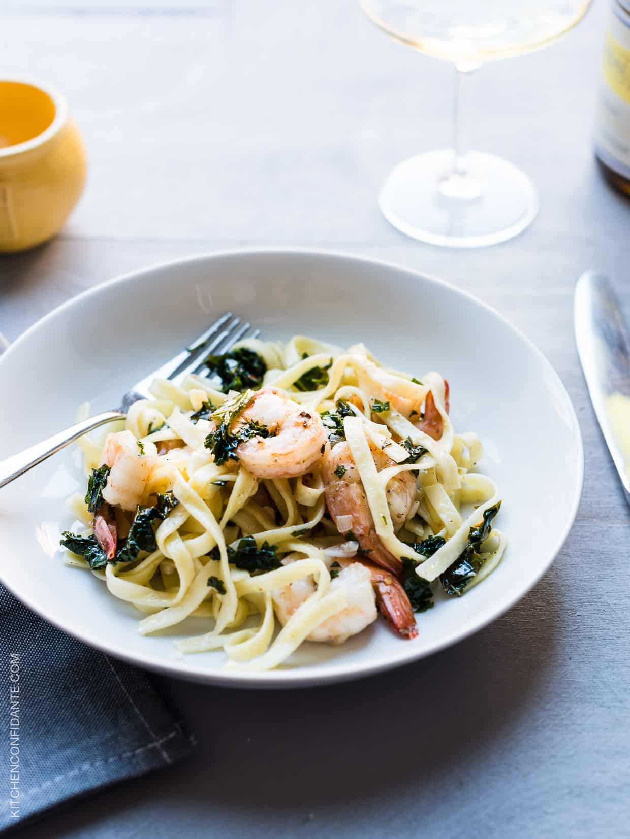 Freshly cooked linguine, leafy kale, and shrimp twirled together on a white dinner plate. 