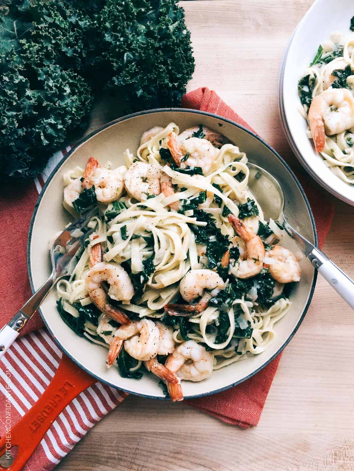 Freshly cooked linguine, leafy kale, and shrimp twirled together on a white dinner plate. 