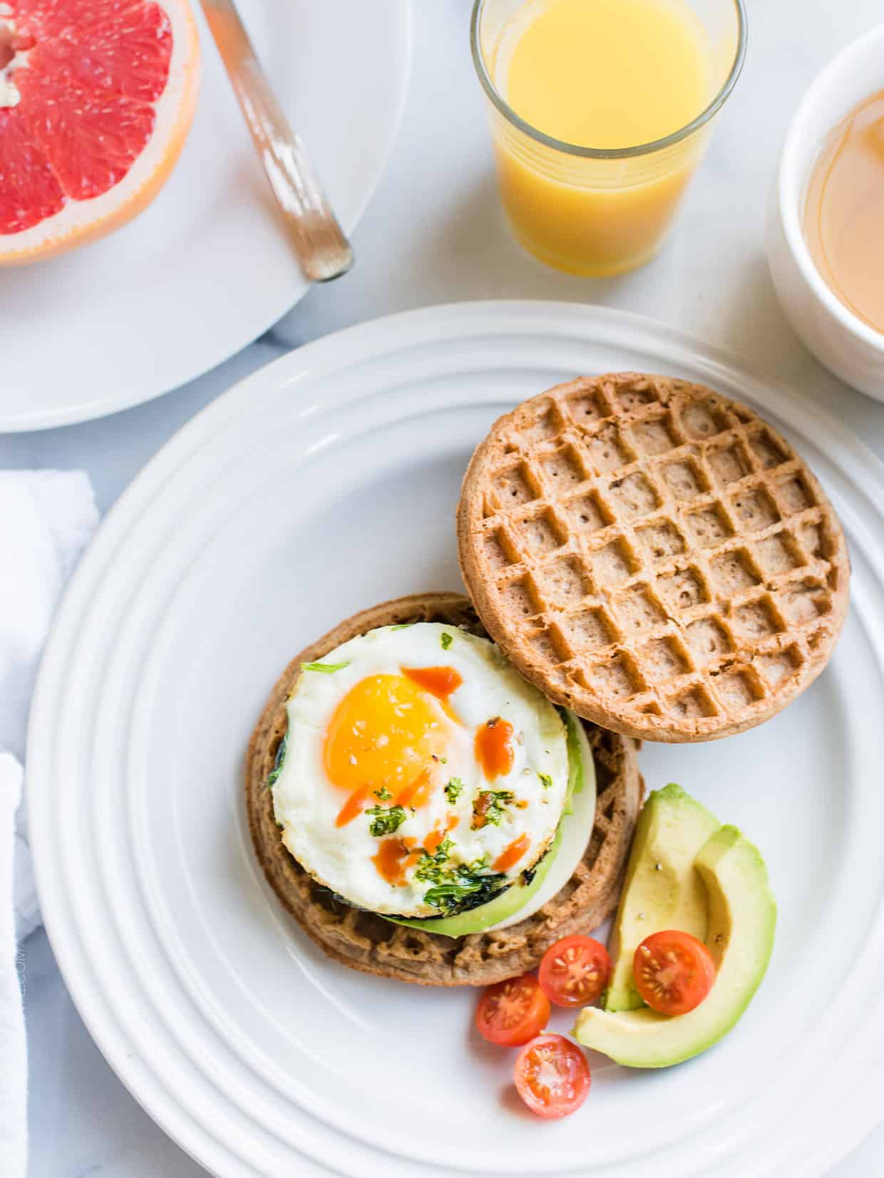 Two wholegrain waffles, one topped with an over easy egg, spinach, avocado, and hot sauce.