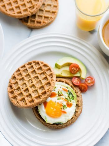 Two wholegrain waffles, one topped with an over easy egg, spinach, avocado, and hot sauce to form a Waffle Breakfast Sandwich.