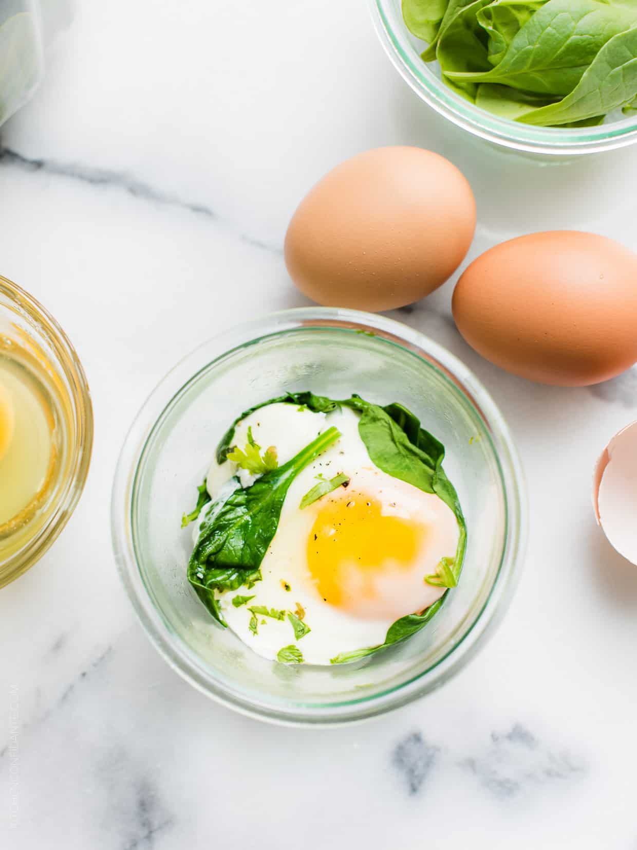 Egg and spinach in a mason jar surrounded by more fresh eggs on a marble surface.