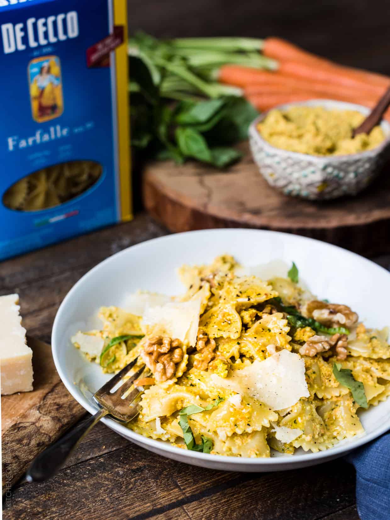 Farfalle with Roasted Carrot Pesto garnished with toasted walnuts and Parmesan cheese on a white plate.